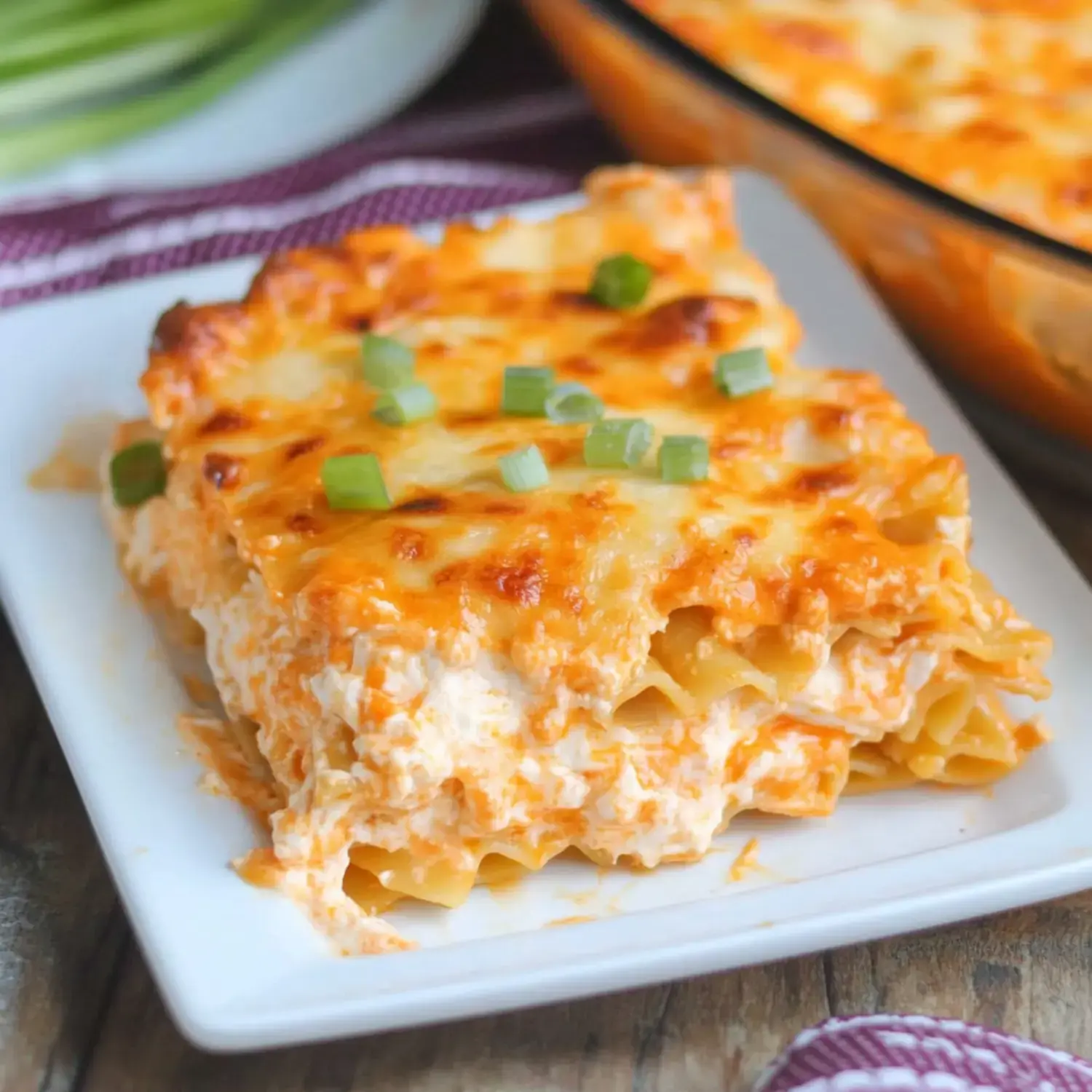 Close-up of creamy layered pasta loaded with chicken and cheese, served on a plate with green onions sprinkled.