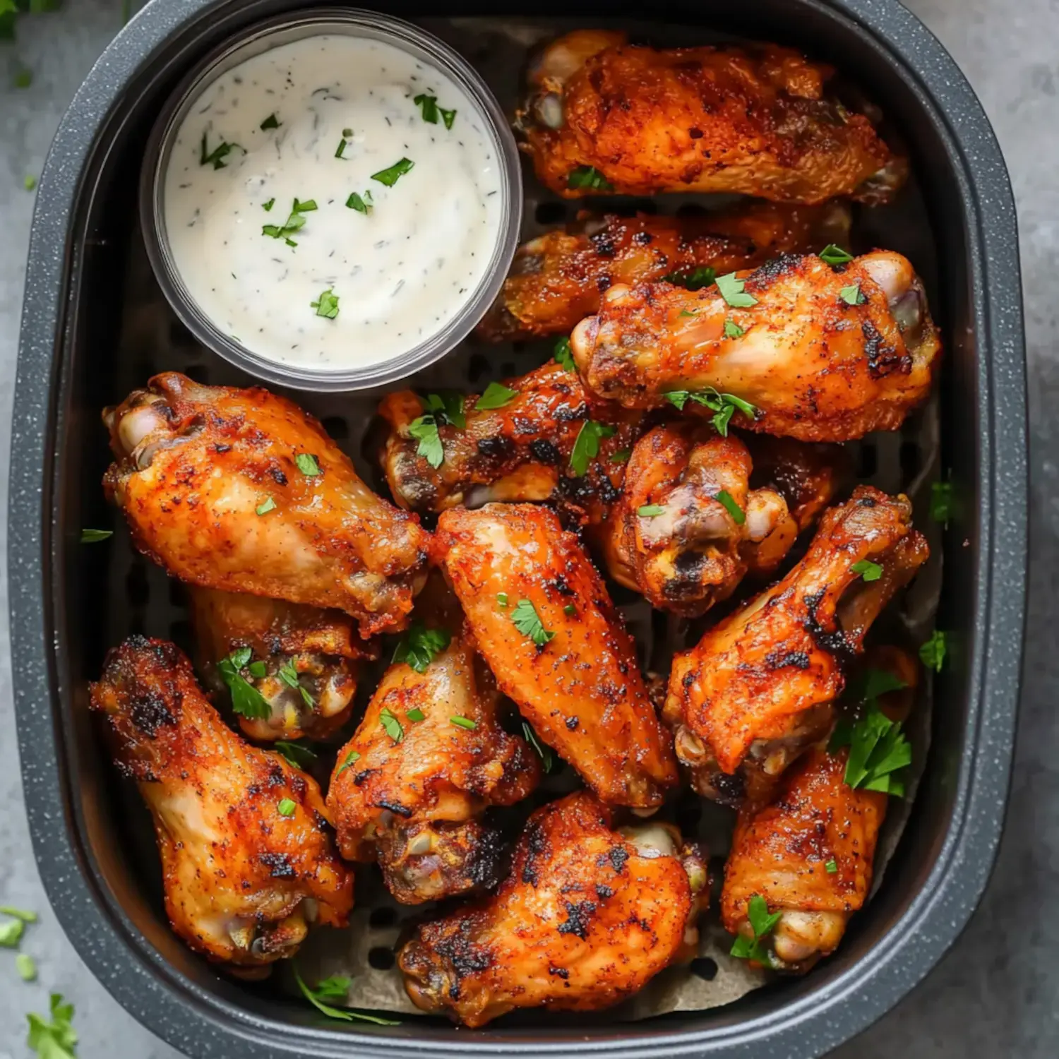 A plate full of golden-crisp wings with herbs and a small bowl of dipping sauce nearby.