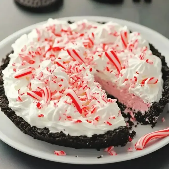 A cheerful chocolate crust peppermint pie with whipped cream and crushed candy toppings, with one slice removed.