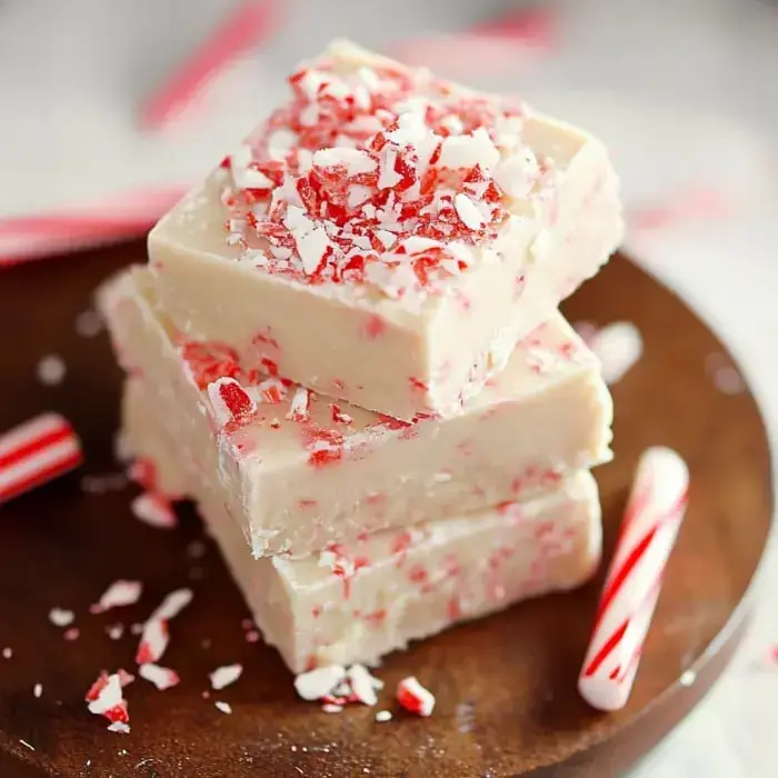 Creamy white fudge with crushed candy cane topping, stacked on a wood tray with candy canes.