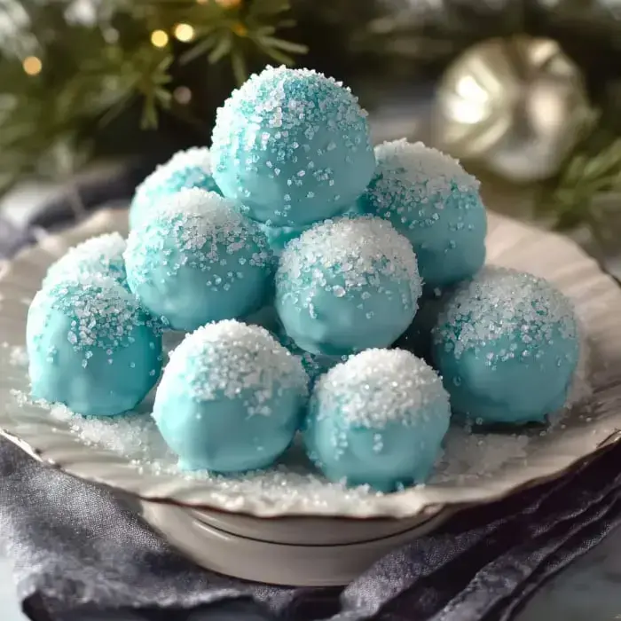 A festive display of sugar-coated, light blue dessert balls that sit on a plate surrounded by holiday greenery.