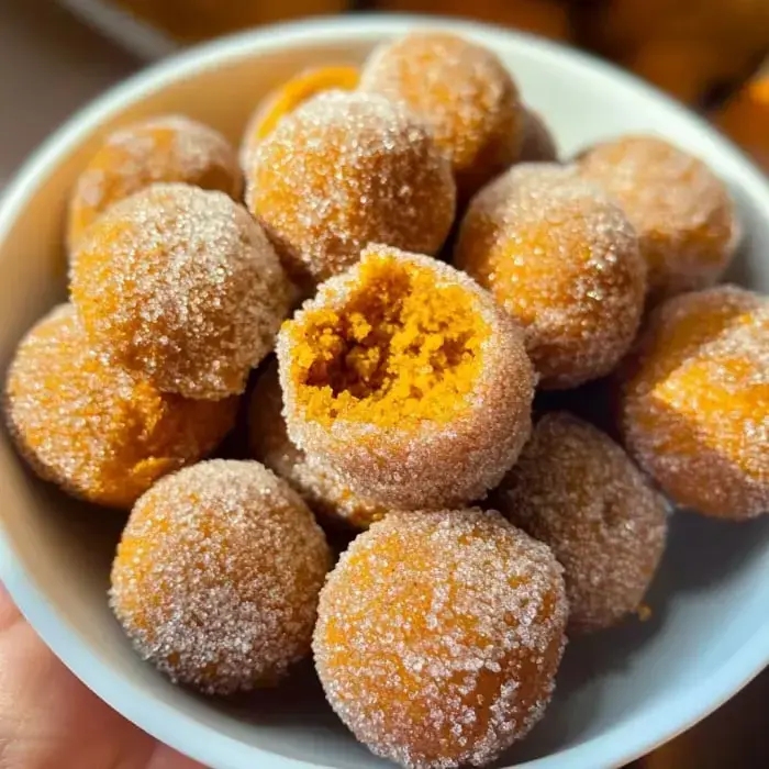 A bowl of orange sugar-coated bites, one missing a bite showing the soft center.