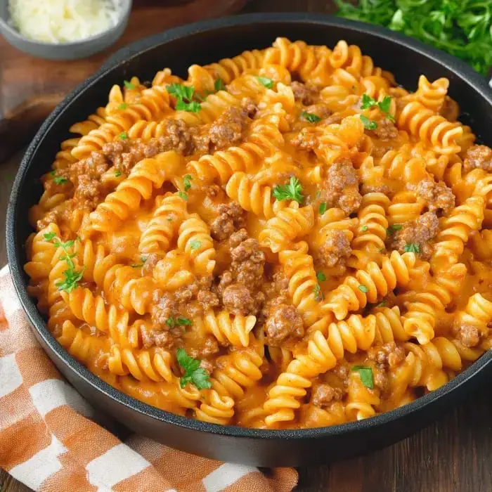 Close-up of spiral pasta covered in a cheesy tomato sauce with ground beef, garnished with parsley.