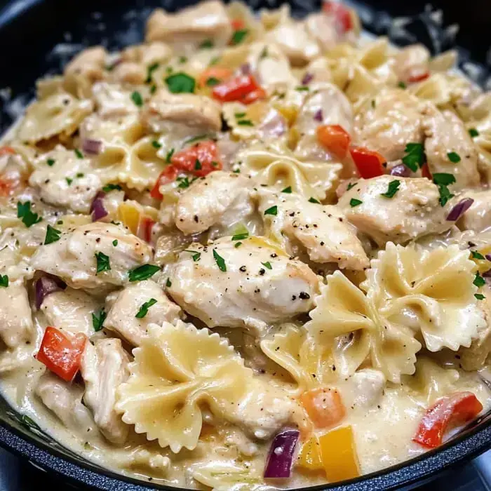 Close view of creamy chicken pasta with bowtie pasta, chopped veggies, and sprinkled parsley.