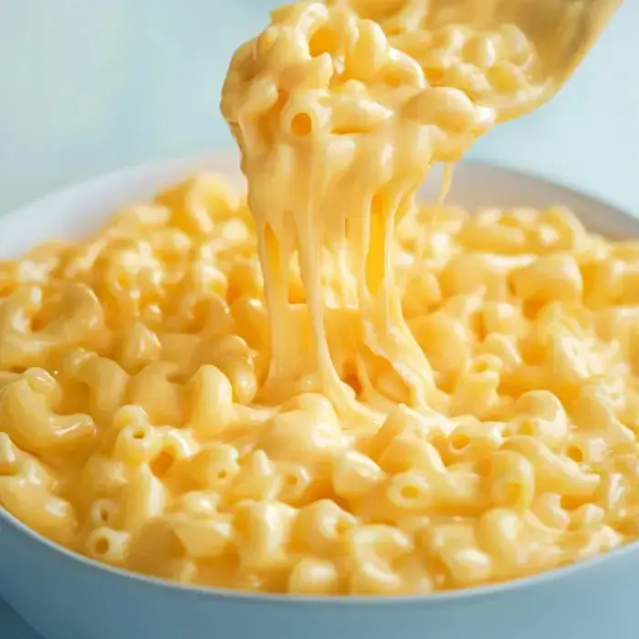 A spoonful of gooey macaroni and cheese lifted from a bowl, showing melted cheese strands.