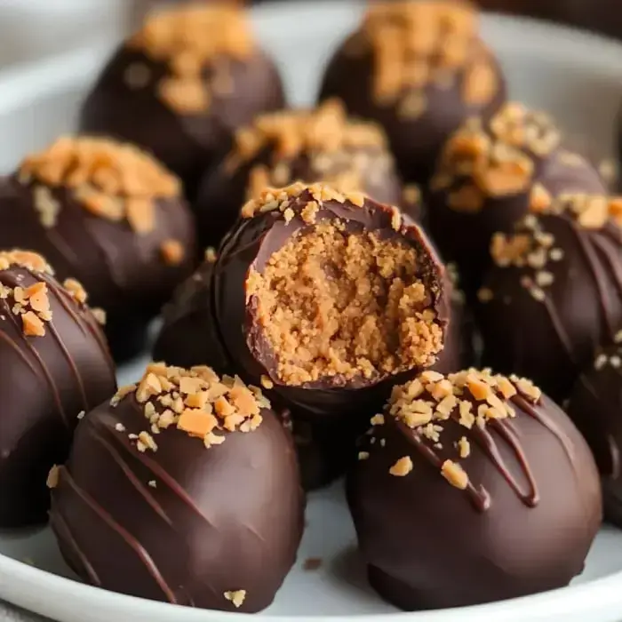 Close-up of chocolate-covered dessert balls, some garnished with crushed nuts, with one ball bitten into, revealing a soft center.