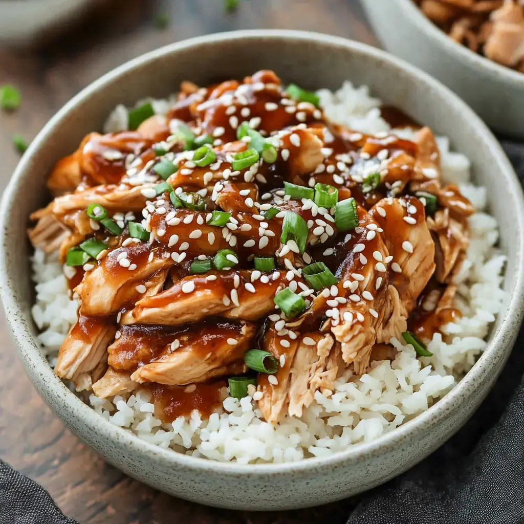 Shredded chicken with sesame seeds and green onions served on white rice with a shiny sauce drizzle.