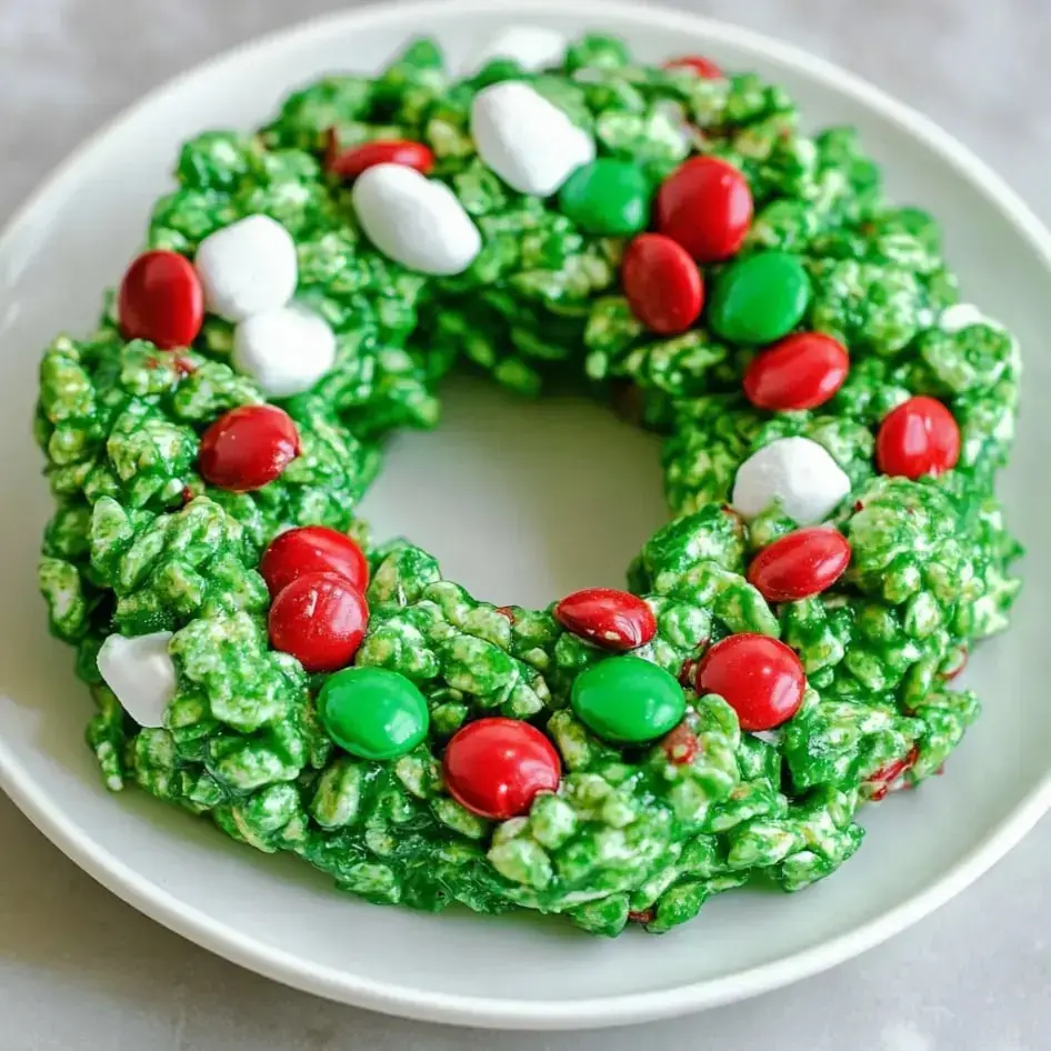 A bright green wreath-shaped cookie decorated with colorful candies and mini marshmallows on a serving dish.
