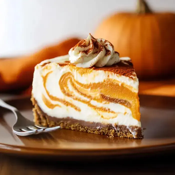 A rich pumpkin cheesecake slice swirled with cream, adorned with whipped topping, set amidst fall decorations.