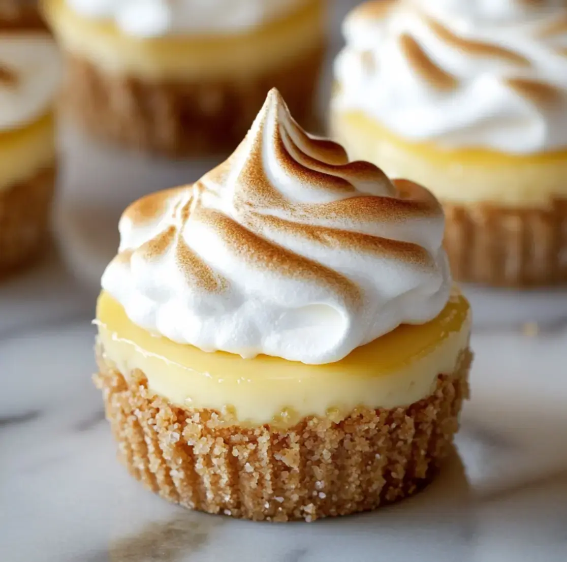 Close view of mini lemon cheesecake with graham base and golden-brown meringue topping.