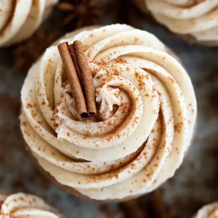 Close-up of a cupcake topped with cinnamon sticks and sprinkled with cinnamon powder.