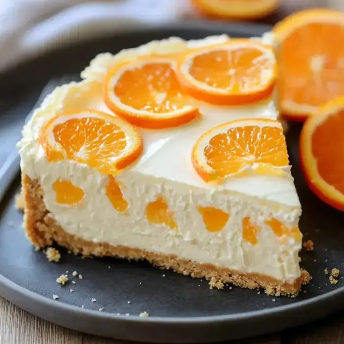 A creamy orange dessert slice garnished with fresh citrus on a dark plate.