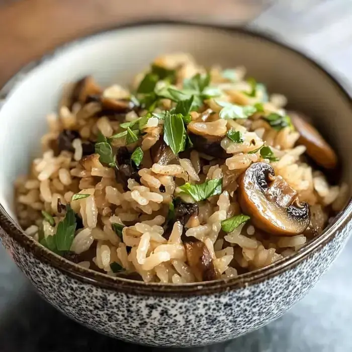 A bowl of fluffy rice mixed with browned mushrooms and topped with fresh parsley.