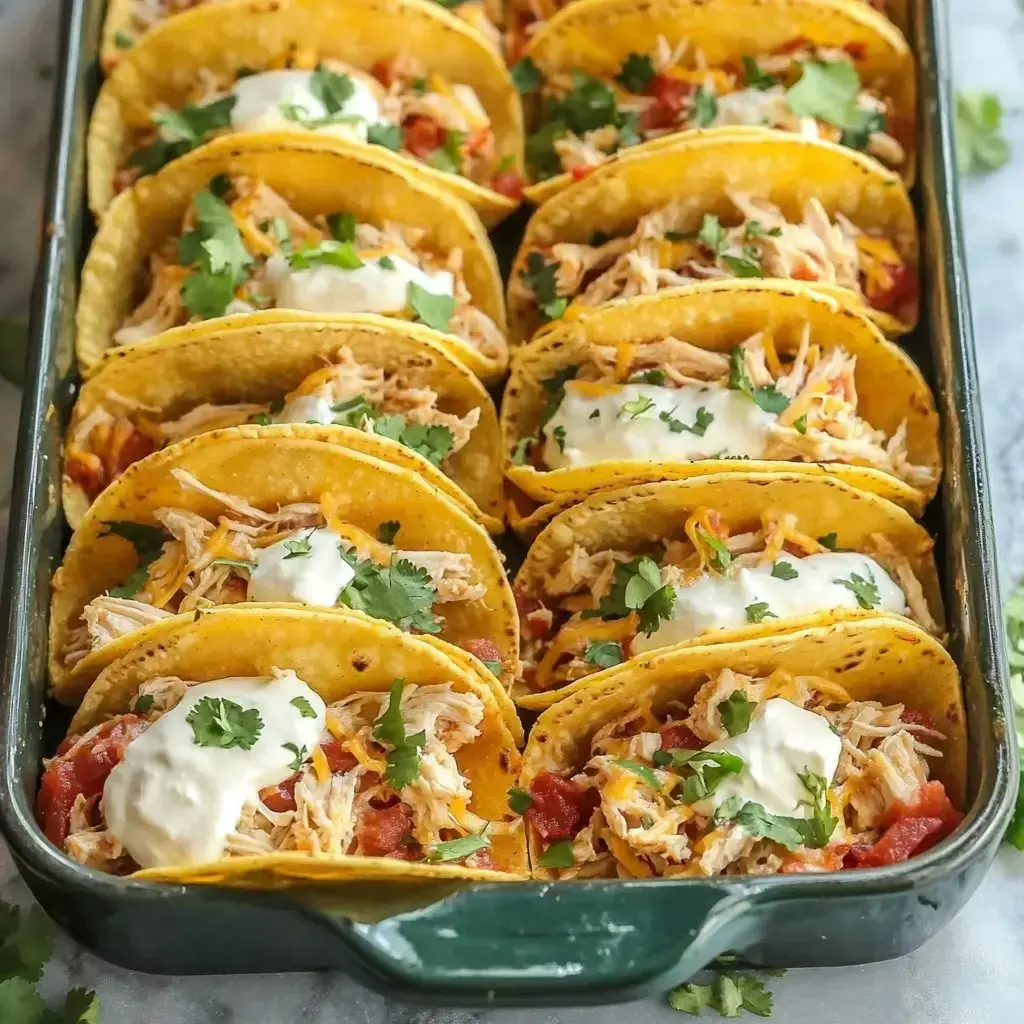 A tray holding baked tacos filled with shredded chicken, cheese, fresh cilantro, tomatoes, and a dollop of sour cream.