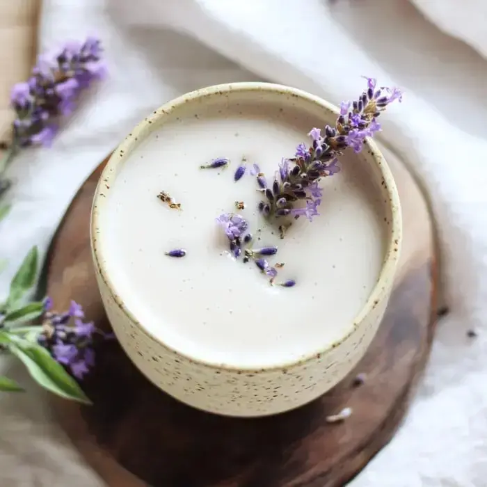 Looking down at a smooth, creamy drink topped with fresh lavender sprigs in a speckled mug on wood.