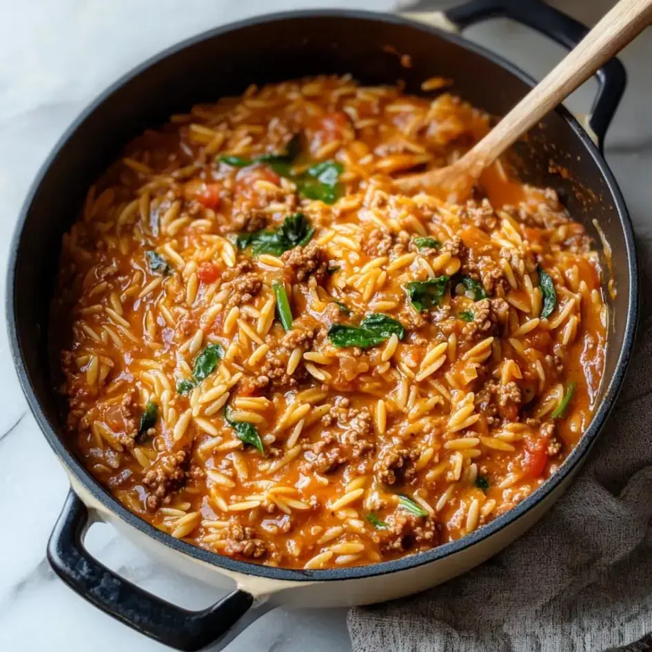 A big pot filled with creamy orzo pasta, ground beef, spinach, and tomatoes.