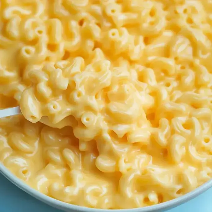 Close-up look at a bowl packed with creamy mac and cheese, spoon lifting a cheesy bite out.