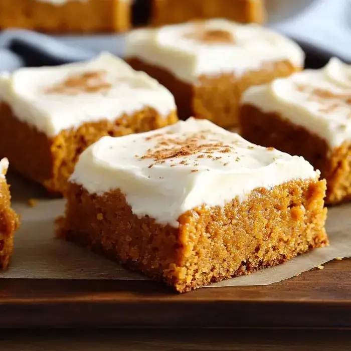Pumpkin bars slathered in cream cheese frosting, sprinkled with cinnamon, sitting on a wooden serving board.
