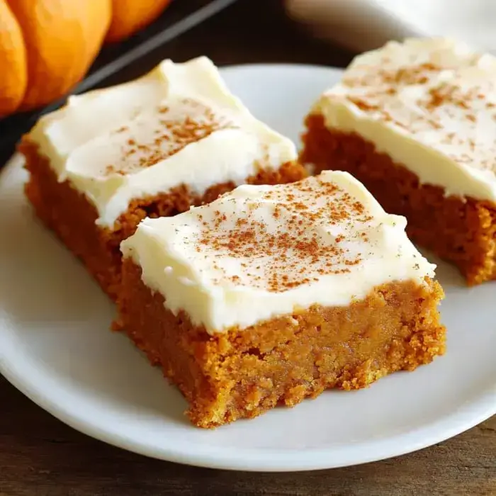 A plate piled with pumpkin bars slathered in creamy frosting and dusted with cinnamon.