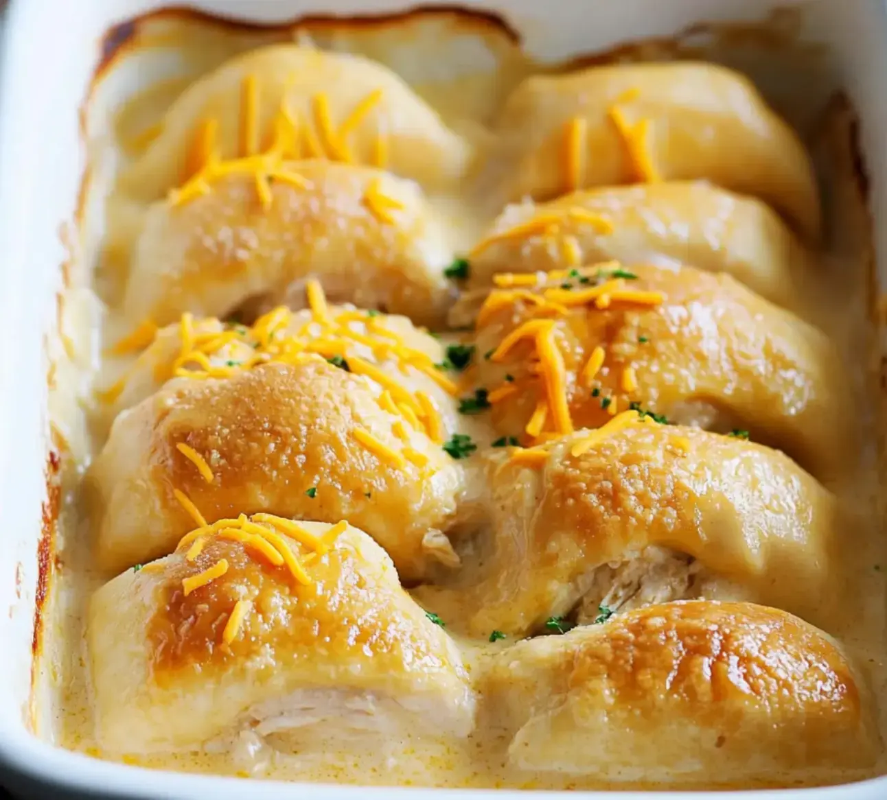 Golden crescent rolls stuffed with chicken and cheese, topped with creamy sauce and a sprinkle of parsley.
