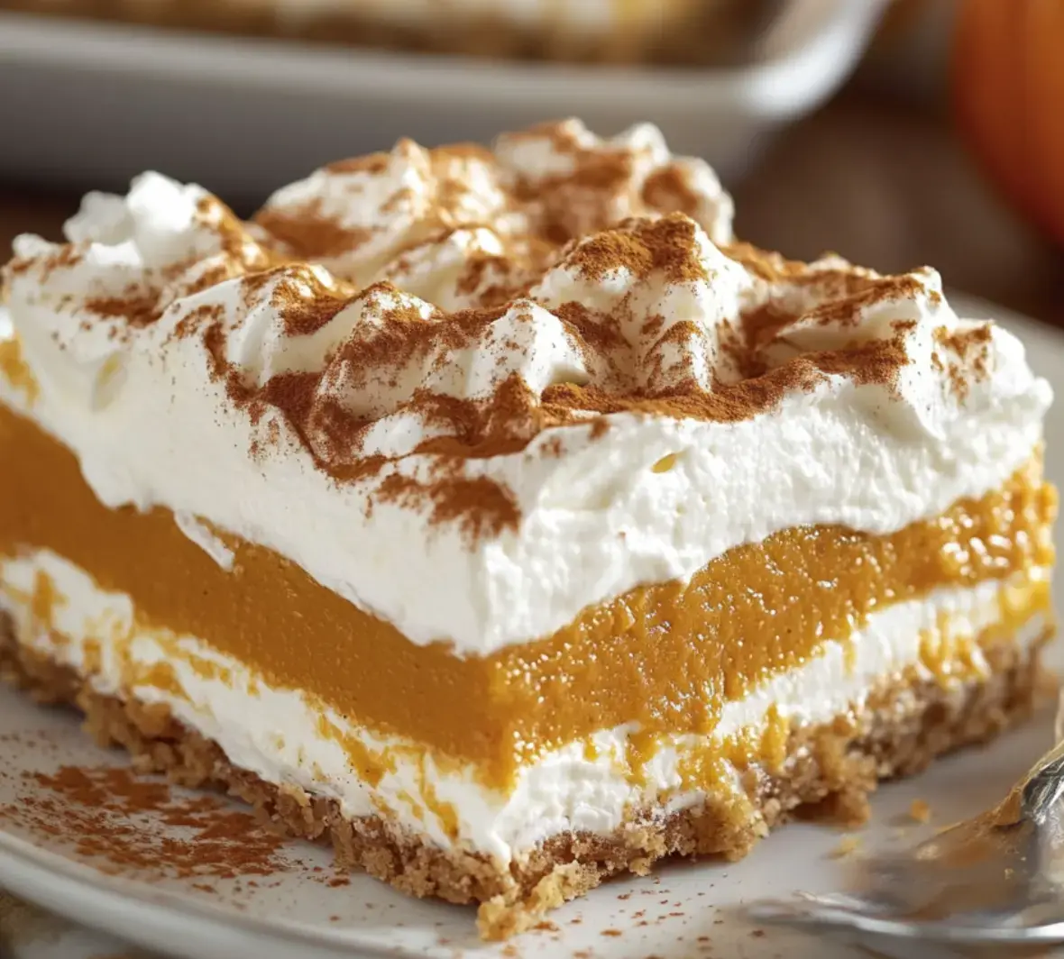 Up close, you see pumpkin filling and whipped cream stacked together, sitting on a spicy cookie crust with cinnamon dusted on top.
