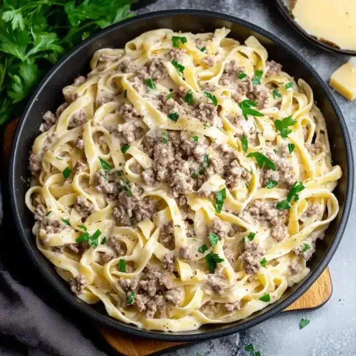 Creamy fettuccine noodles piled with savory ground beef and fresh parsley in a cozy bowl.