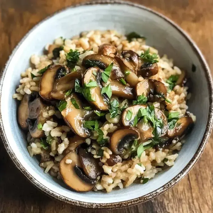 Brown rice in a bowl loaded with sautéed mushrooms and a scatter of parsley on top.