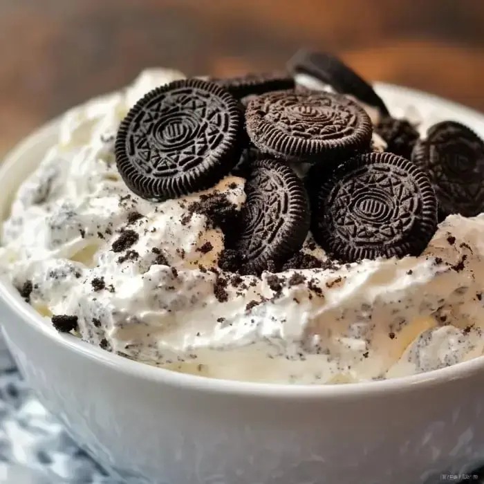 A serving bowl filled with fluffy whipped topping and Oreo cookie bits, garnished with whole Oreos.