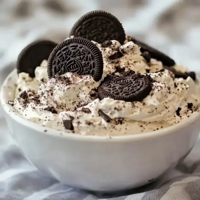 Fluffy whipped dessert with Oreo bits and whole Oreos on top in a bowl.