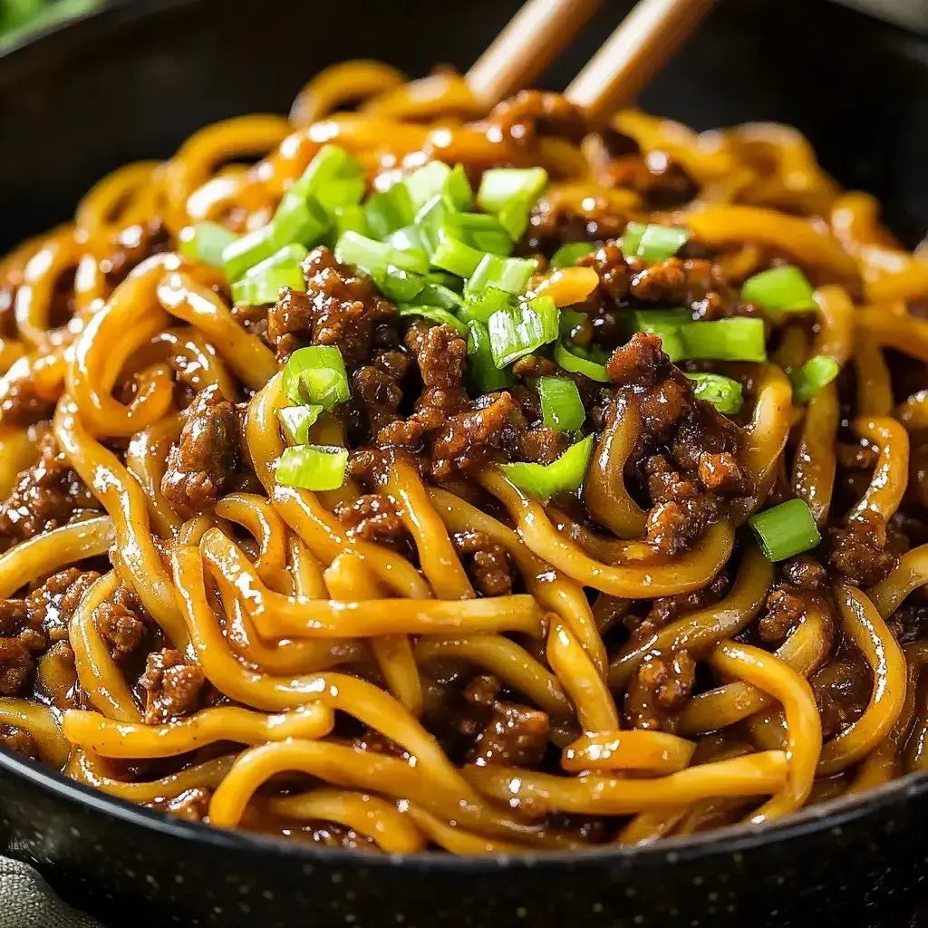 A bowl loaded with saucy noodles, ground beef, and green onions up close.
