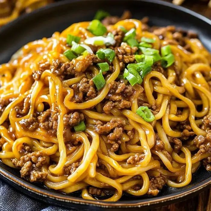 A plate filled with noodles, ground beef, and green onion shot up close.