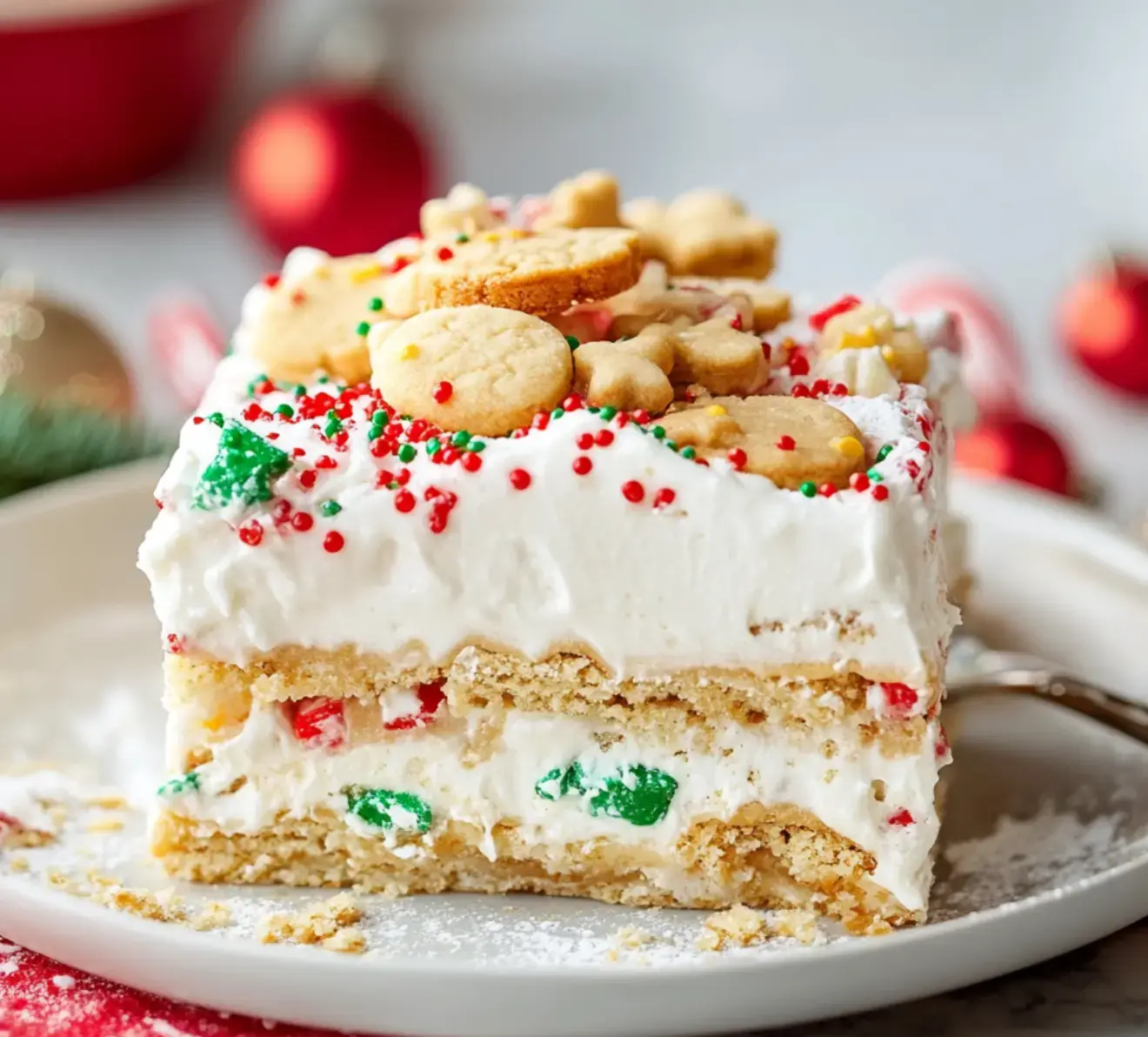 A festive treat stacked with creamy layers, bright sprinkles, and fun-shaped cookies on top sits on a plate.