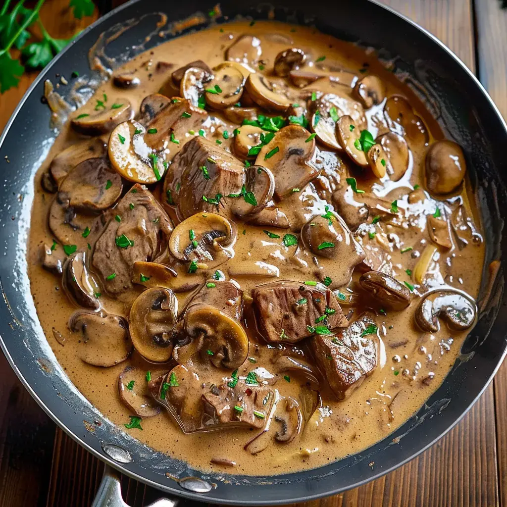 A pan filled with chunks of beef and mushrooms in a creamy sauce, topped with parsley.