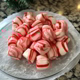 Bright red and white peppermint swirls stacked on a light platter, dusted with sugar.