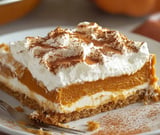 A pumpkin layered dessert with creamy topping and a crumbly spice crust, sprinkled with cinnamon.