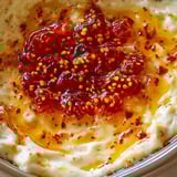 A creamy spread topped with glossy red jelly and mustard seeds.