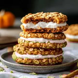Stacked oatmeal cookies with cream filling, one showing a bite on a gray plate.