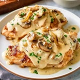 Grilled chicken breasts topped with sautéed mushrooms and onions, garnished with parsley.