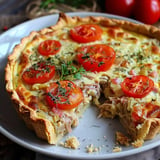 A savory pie loaded with tomatoes, herbs, and chunks of tuna, with a slice removed.