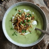 A green soup topped with chopped chives, pine nuts, and crispy onions, served in a bowl.