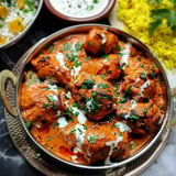 A dish of creamy curry chicken garnished with coriander and served alongside golden rice.